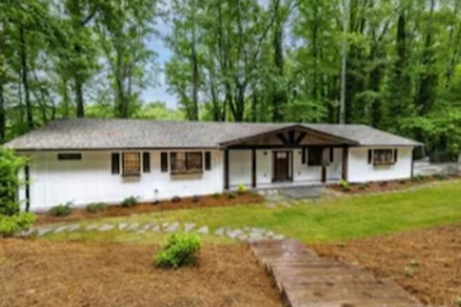 Long white ranch home set back under mature trees at 309 Woodland Way in Clemson, South Carolina